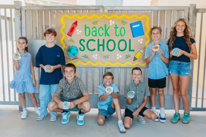 Group of smiling kids holding &iexcl;Yo Quiero! Grab & Go dips in front of a colorful &ldquo;Back to School&rdquo; sign.