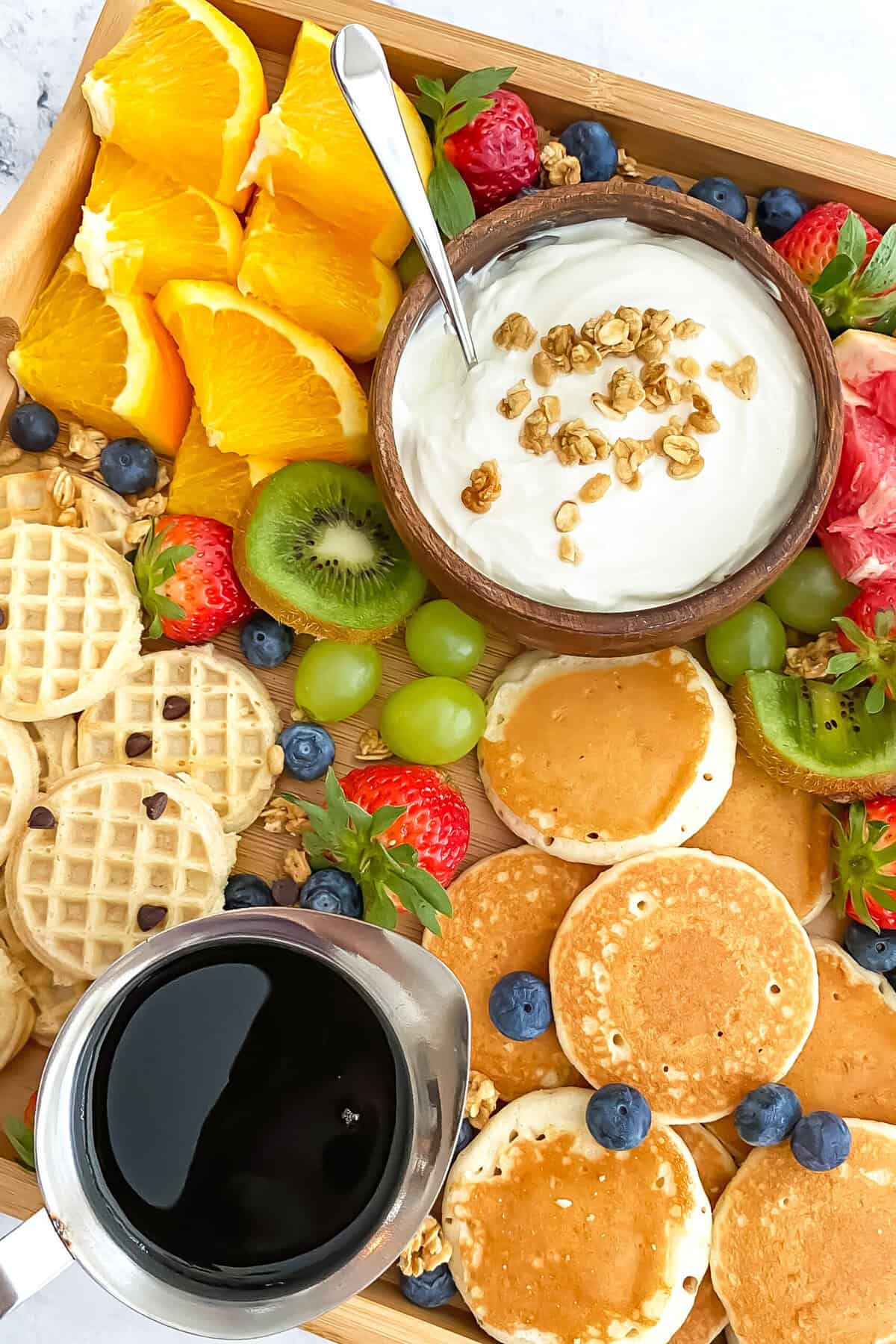 Yogurt, fruit, and pancakes on a breakfast board.