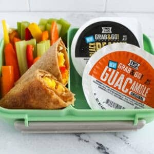 Healthy breakfast for kids with egg and veggie taquitos, colorful bell pepper sticks, and &iexcl;Yo Quiero! Grab & Go guacamole and bean dip cups in a lunchbox